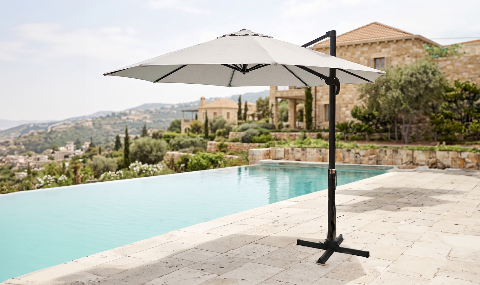 Modern outdoor umbrella positioned beside a swimming pool overlooking a sunlit Mediterranean-style landscape